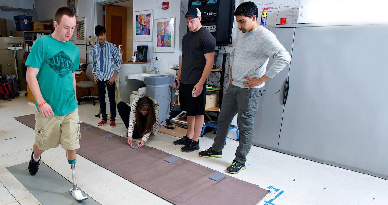 Students watch a man walk on a prosthetic leg